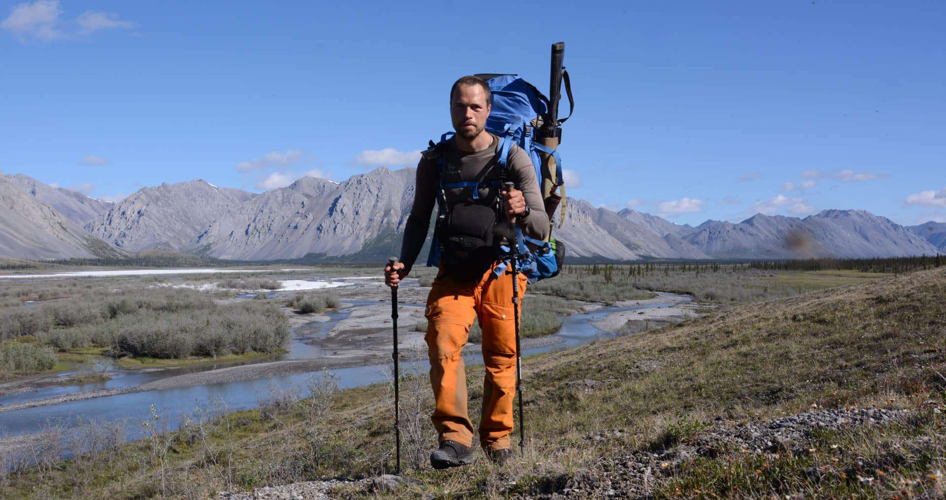 Erik B. Jørgensen vandre med stor rygsæk, gevær og vandrestav, i storslået langskab under "Alaska på tværs"