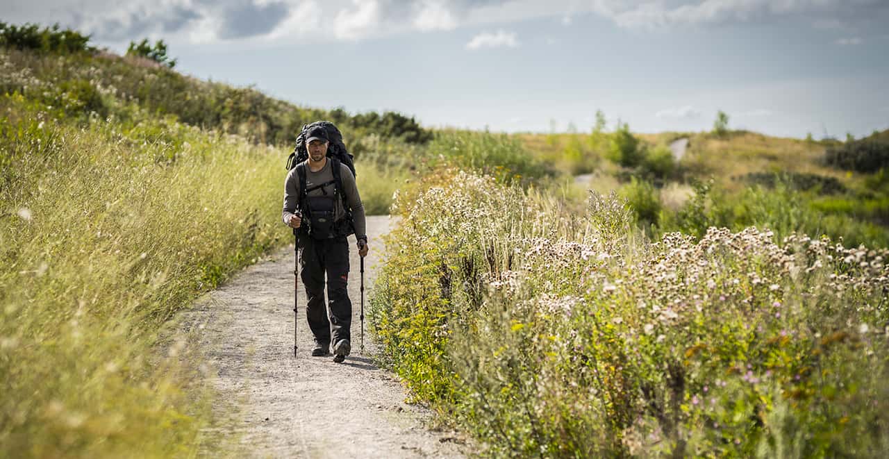 Erik B. Jørgensen på vandretur, går med rygsæk, fototaske foran og vandrestave