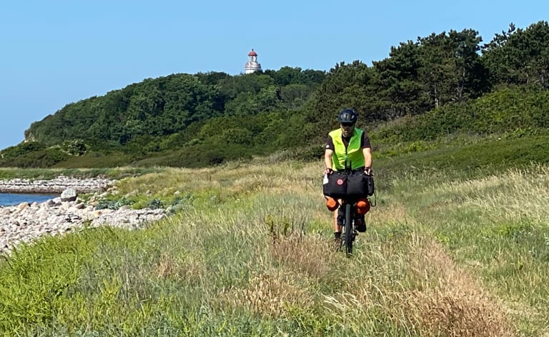 Erik B. Jørgensen cykler på stranden, fyr i baggrunden, under Bikepacking, Danmark rundt