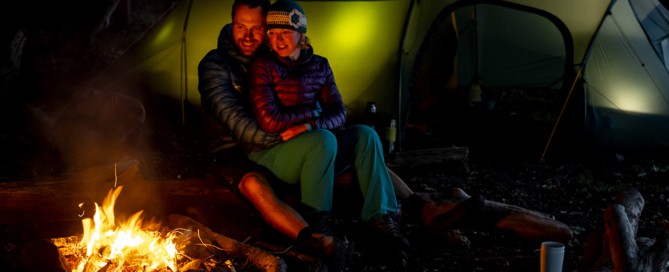 Erik B. Jørgensen og Tine Henriksen sidder op ad hinanden ved bålet, telt i baggrund. Titel: Hygge i den danske natur, med Erik B. Jørgensen. Foto Rene Schütze