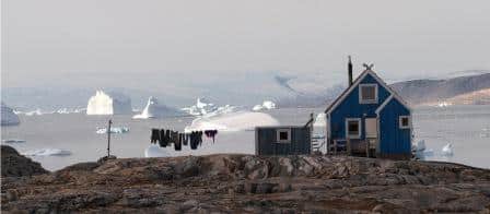 Tur til Østgrønland. Hus i Isortoq, med indlandsisen i baggrunde og isbjerge i havet.